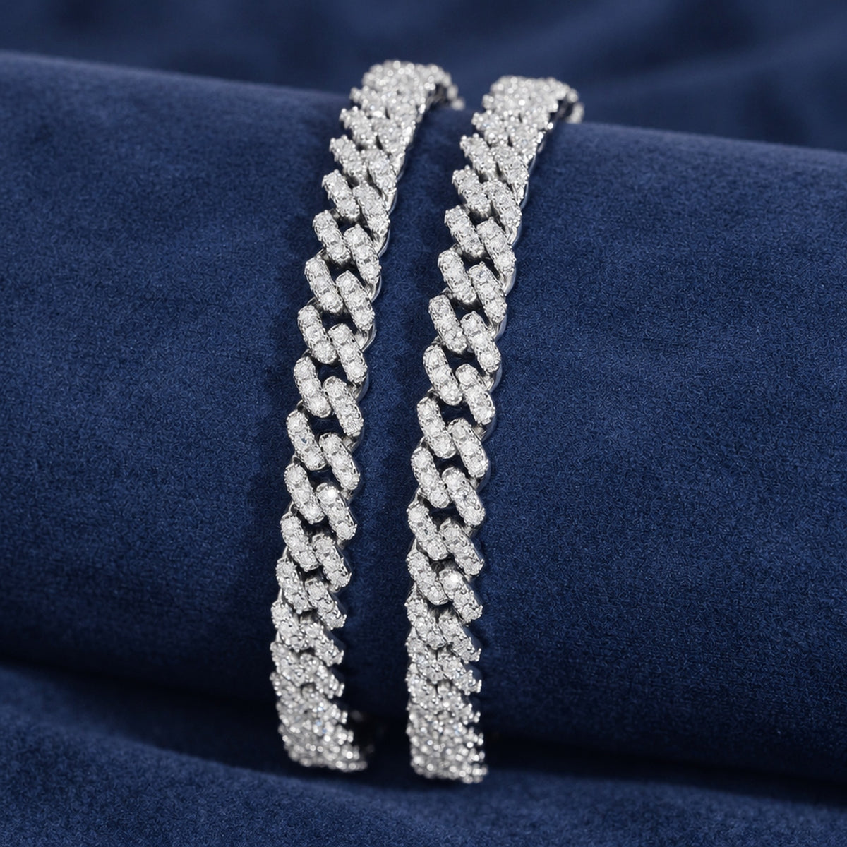 Two 6mm iced Cuban link bracelets in 925 silver draped over a navy suede block
